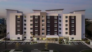 Un hotel de varios pisos con diseño moderno, que presenta una entrada central con área cubierta y un estacionamiento con espacios delimitados.