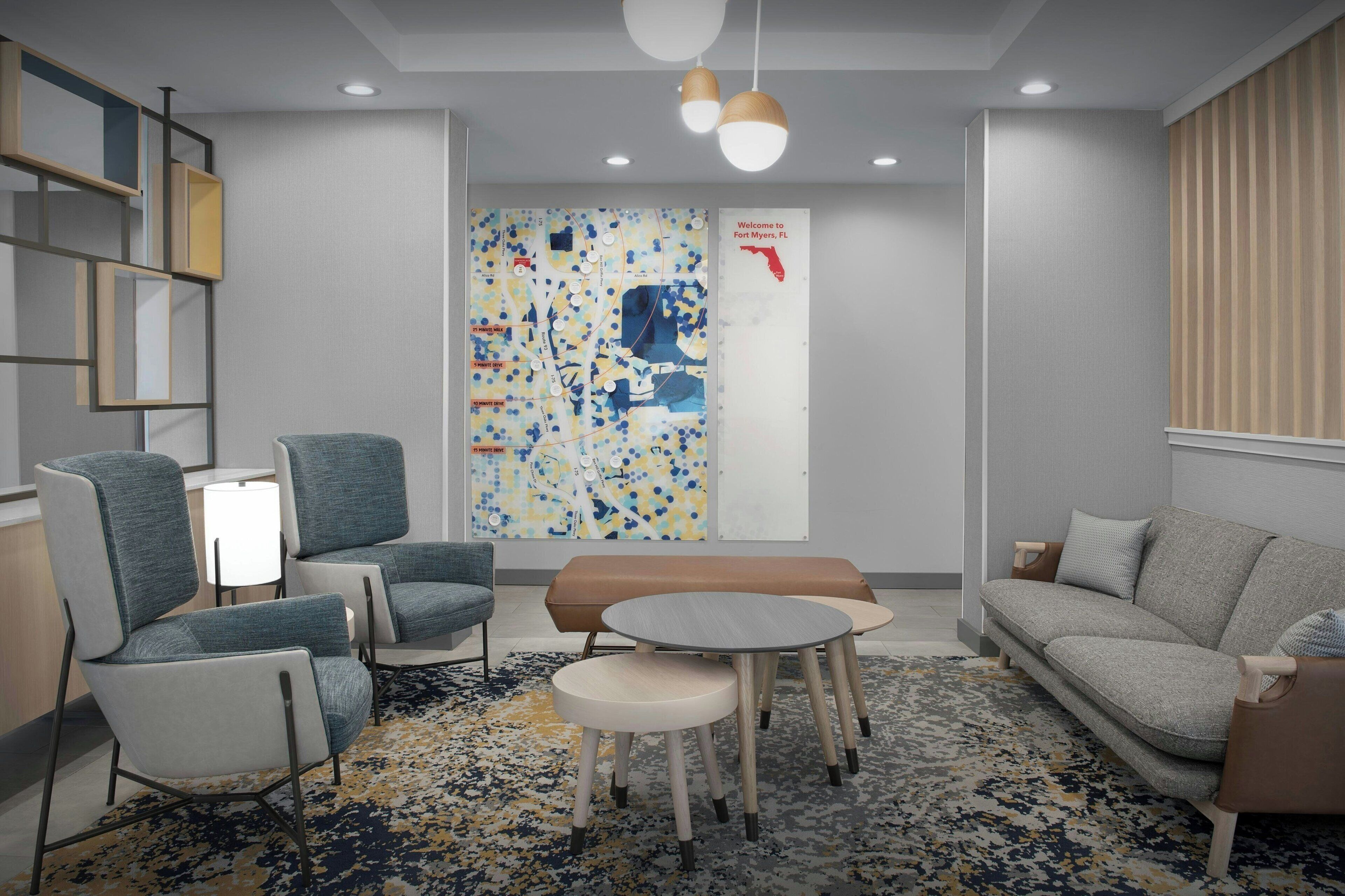 A modern hotel lobby with a large abstract wall art, seating arrangements, and a map of Fort Myers, FL.