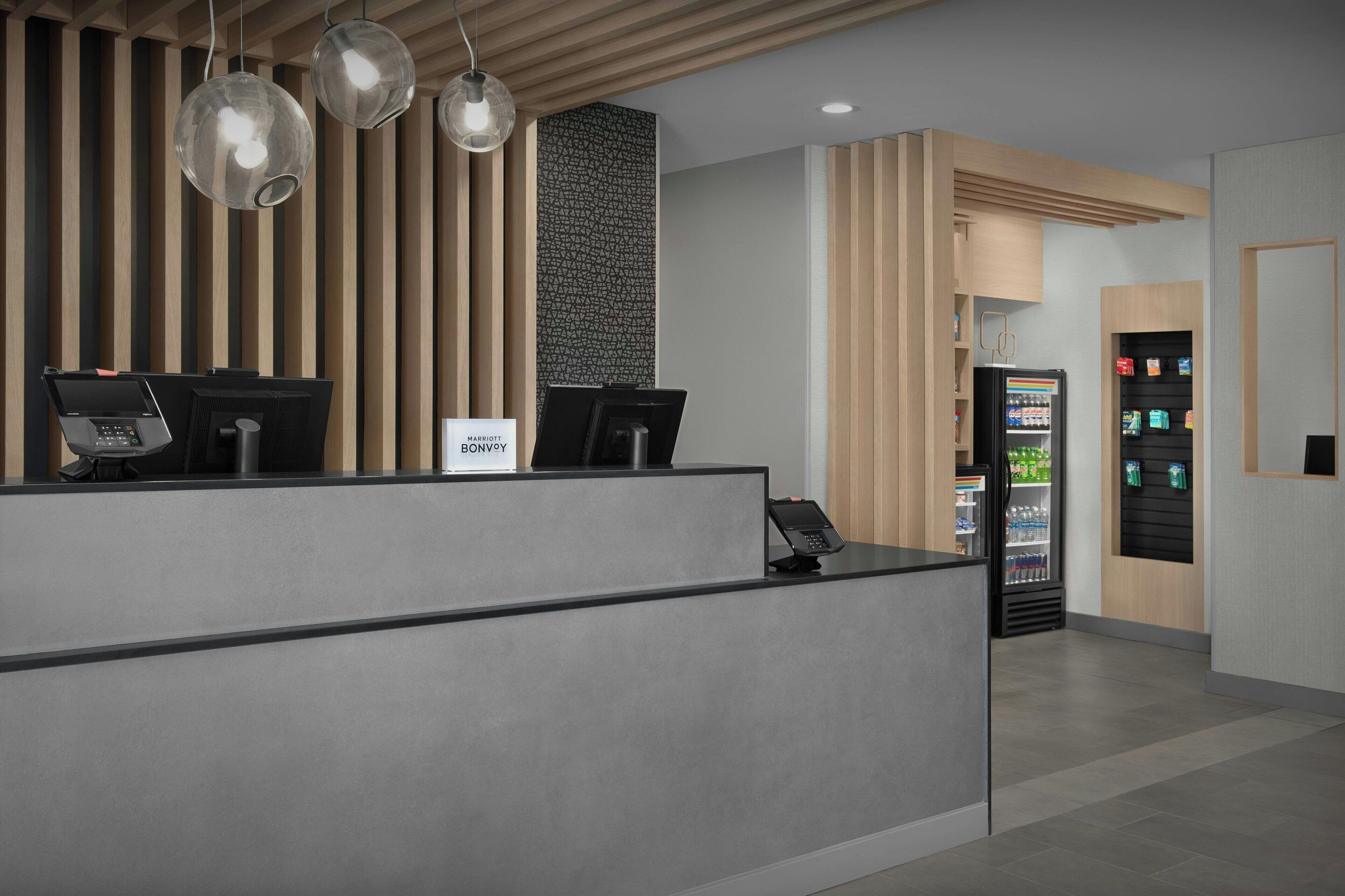 A modern reception desk with two computer stations, a vending machine, and a wall with vertical wooden slats.