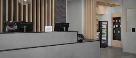 En modern receptionsdisk med två datorarbetsplatser, en automattjänst och en vägg med vertikala träribbor.