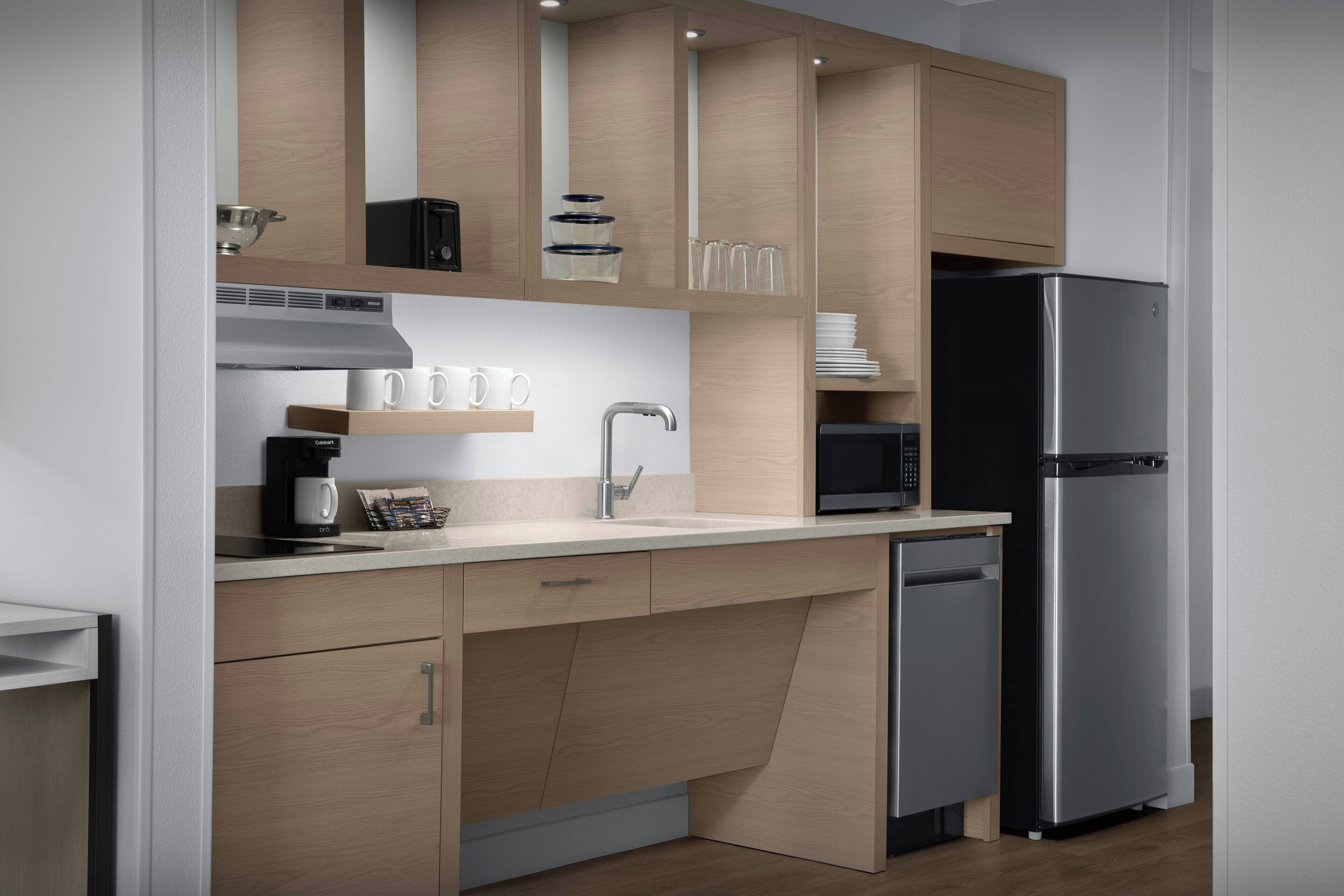 A modern kitchen with wooden cabinets, a stainless steel refrigerator, a microwave, and a coffee maker.