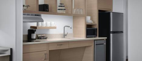 A modern kitchen with wooden cabinets, a stainless steel refrigerator, a microwave, and a coffee maker.