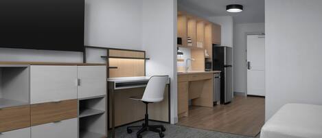 A modern, compact room with a desk, chair, kitchenette, and a bed.