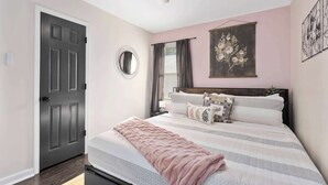 Ein Schlafzimmer mit einem Bett, Deckenventilator, einem Fenster mit Vorhängen und einem wandmontierten Spiegel.