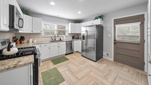 A modern kitchen with white cabinets, stainless steel appliances, and a herringbone wood floor. - Great Home_Roomy_Sleeps 13_Mins To GEHA_Dogs OK (Lee's Summit)