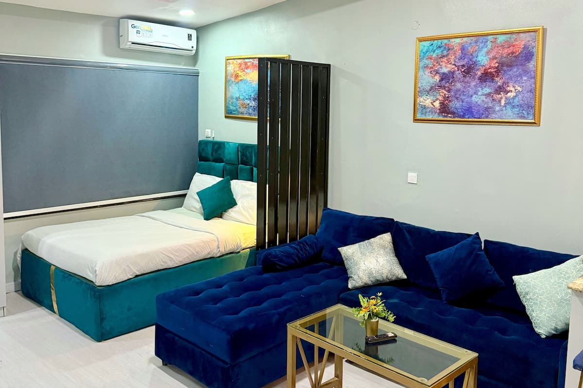 Une chambre à coucher moderne avec un lit, un canapé bleu, une table basse en verre et un tableau au mur.