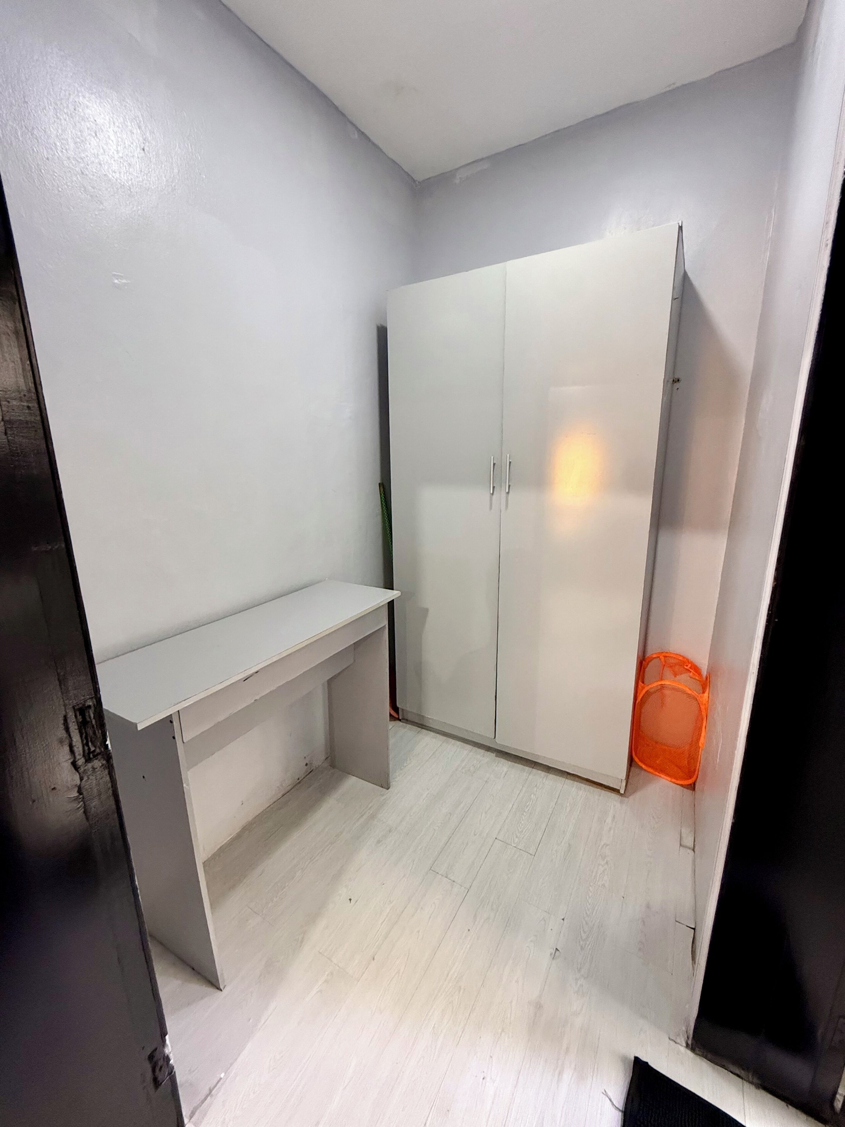 Une pièce avec une armoire blanche, un banc et un petit panier orange.