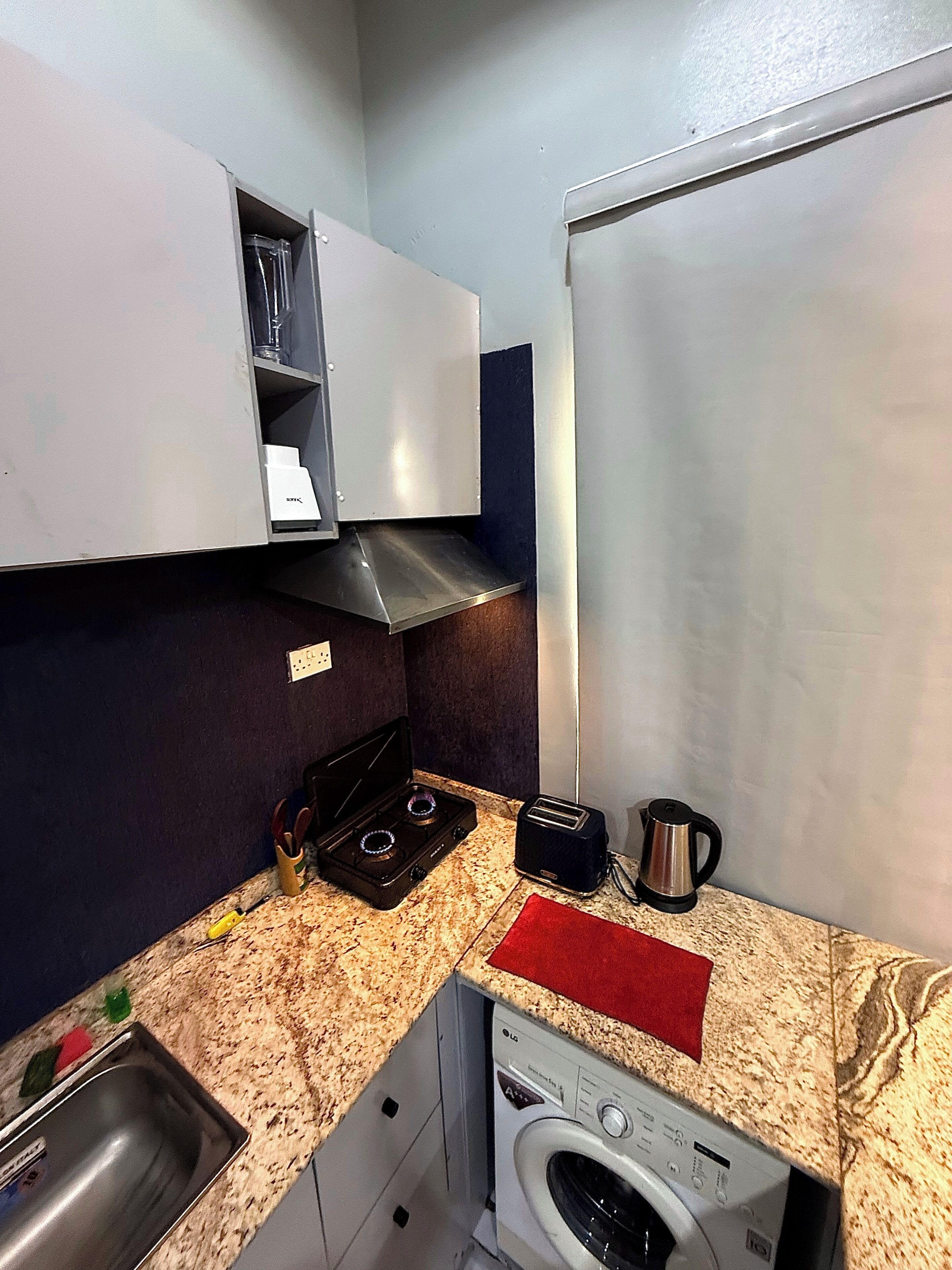 Une cuisine compacte équipée d’une cuisinière à gaz, d’un grille-pain, d’une bouilloire, d’un lave-linge et d’un évier.