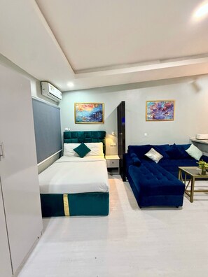 A compact hotel room with a bed, a sofa, two paintings, and a small table. - Open plan studio apartment unit (Lekki)