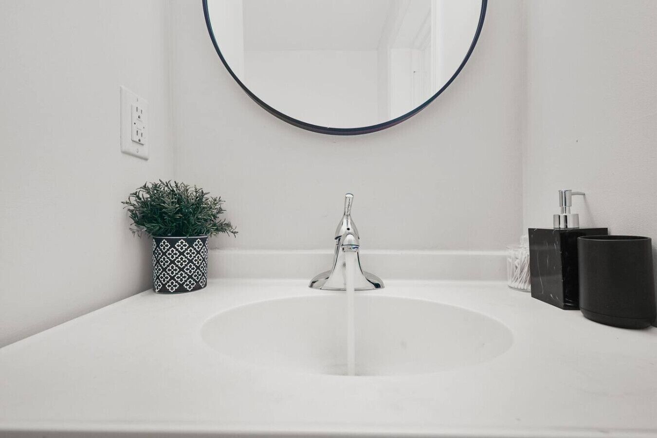 A white bathroom sink with a modern faucet, a potted plant, and toiletries on the counter.