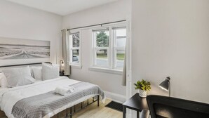 Un dormitorio con cama, mesita de noche, lámpara y ventana con cortinas.