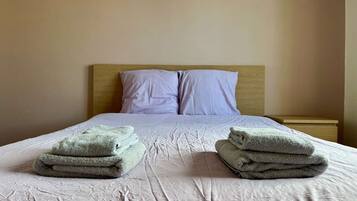A neatly made bed with a wooden headboard, two pillows, and two stacks of folded towels.