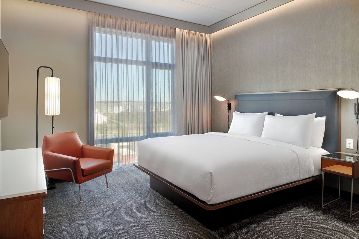 Ein Hotelzimmer mit einem großen Bett, einem Schreibtisch, einem Sessel, einem Nachttisch und einer Lampe.