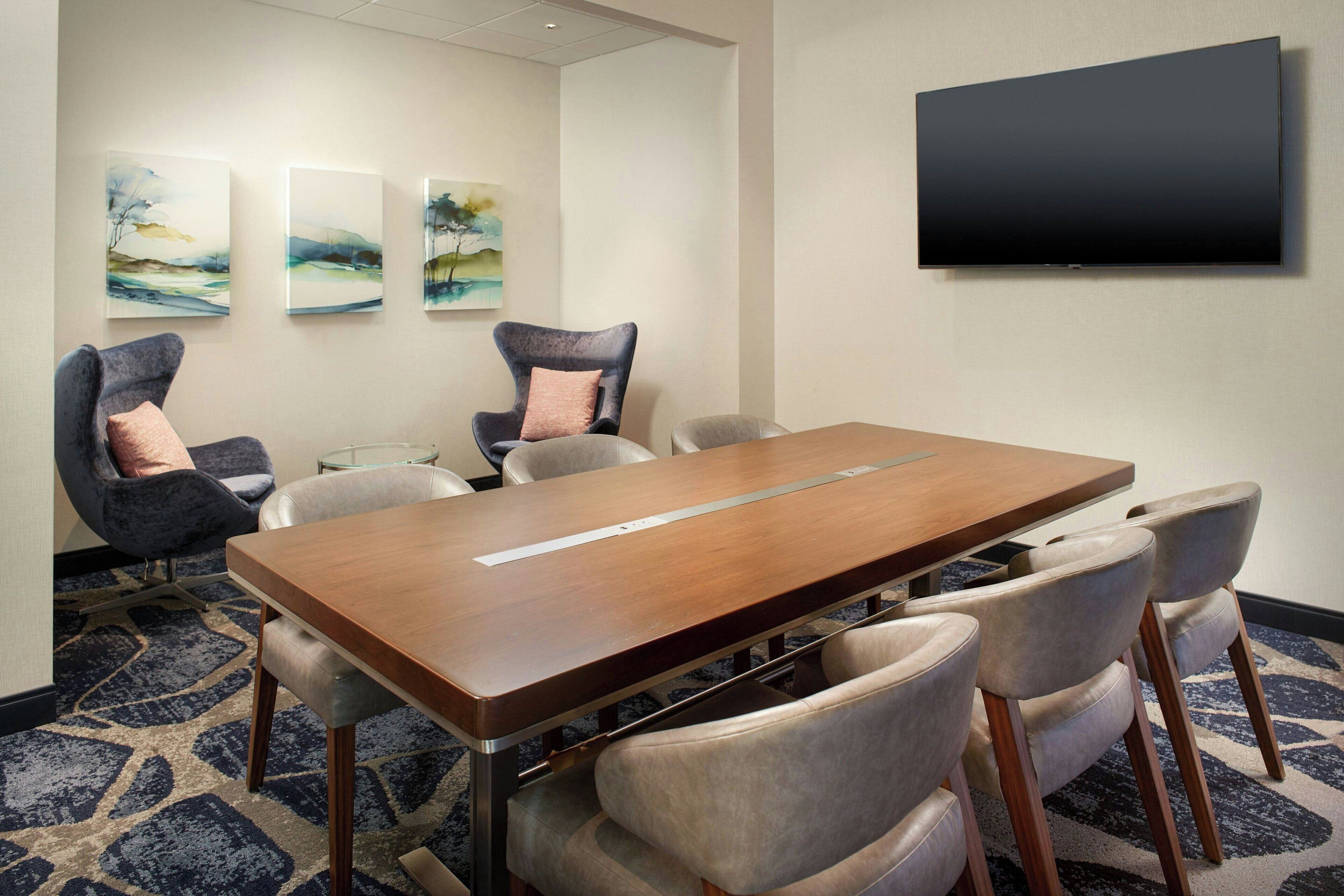 A conference room with a wooden table, six chairs, and three abstract paintings on the wall.
