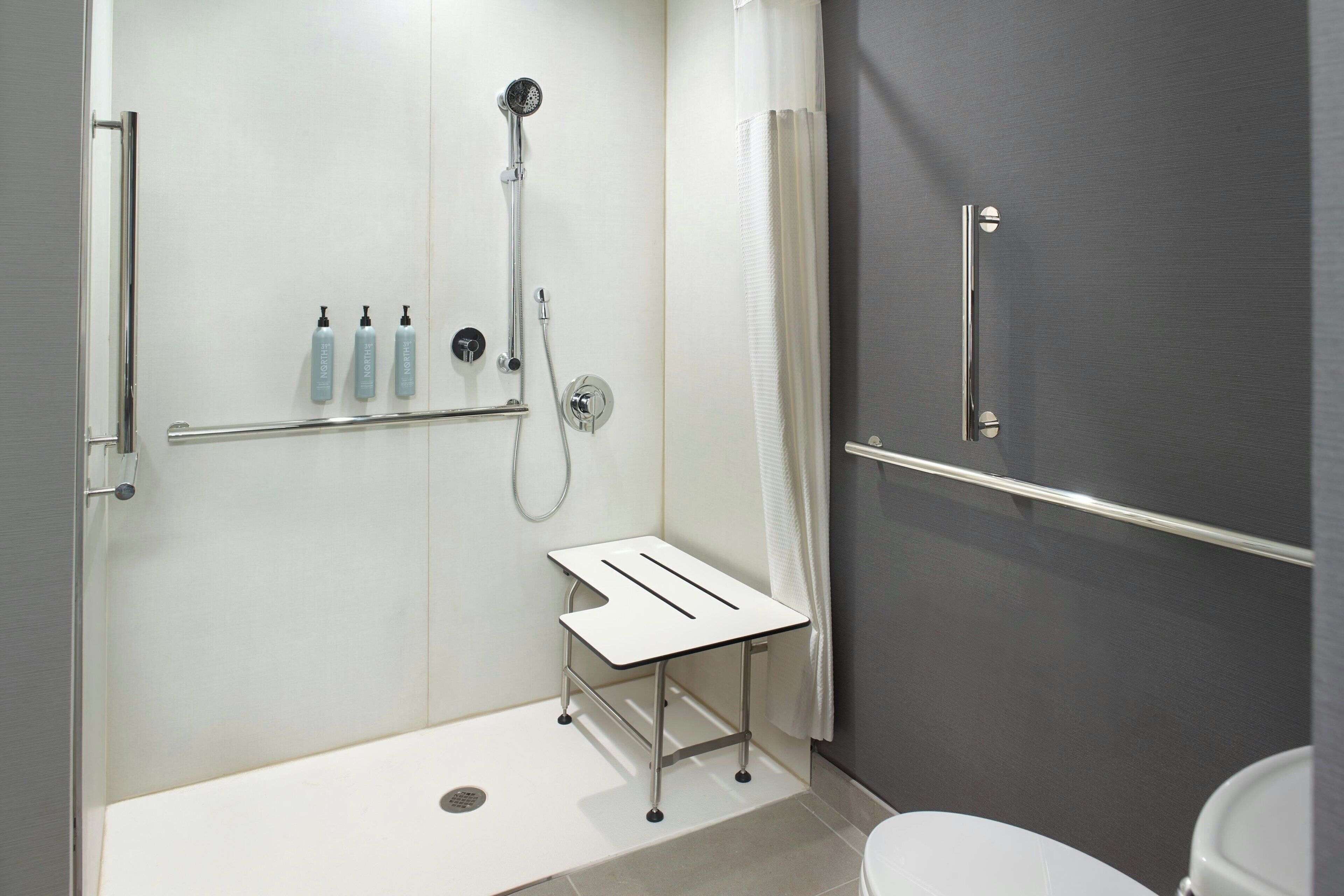 Un baño moderno con ducha, inodoro y una pequeña mesa con botellas.