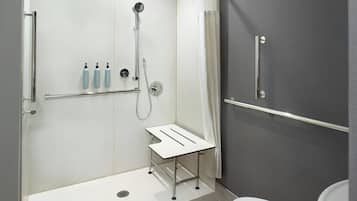 Un baño moderno con ducha, inodoro y una pequeña mesa con botellas.
