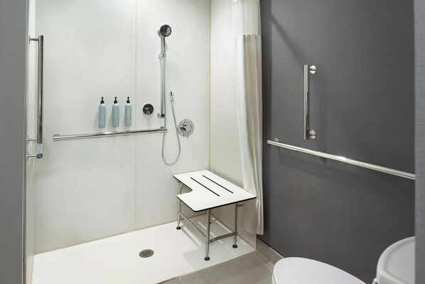 A modern bathroom with a shower, toilet, and a small table with bottles.