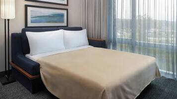 Una habitación de hotel con cama, mesita de noche, lámpara y ventana con cortinas.