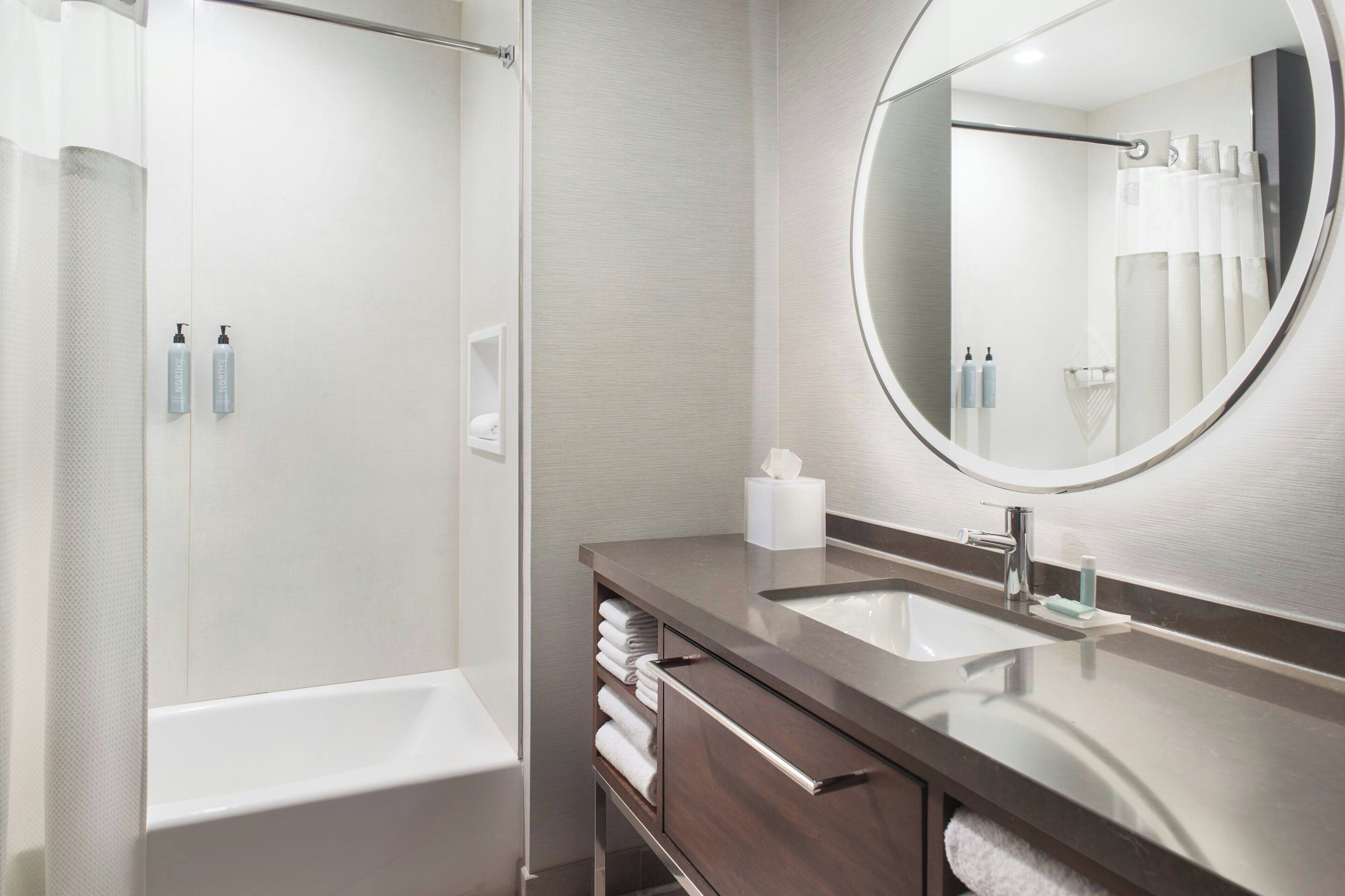 A modern bathroom with a bathtub, a large mirror, and a vanity with a sink.