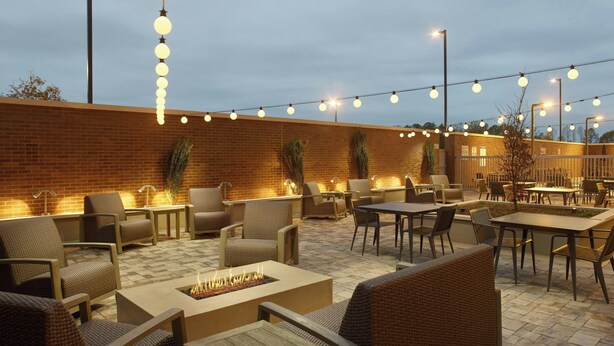 Eine Außenpatio-Terrasse mit Korbmöbeln, einem Feuerkorb und Lichterketten.