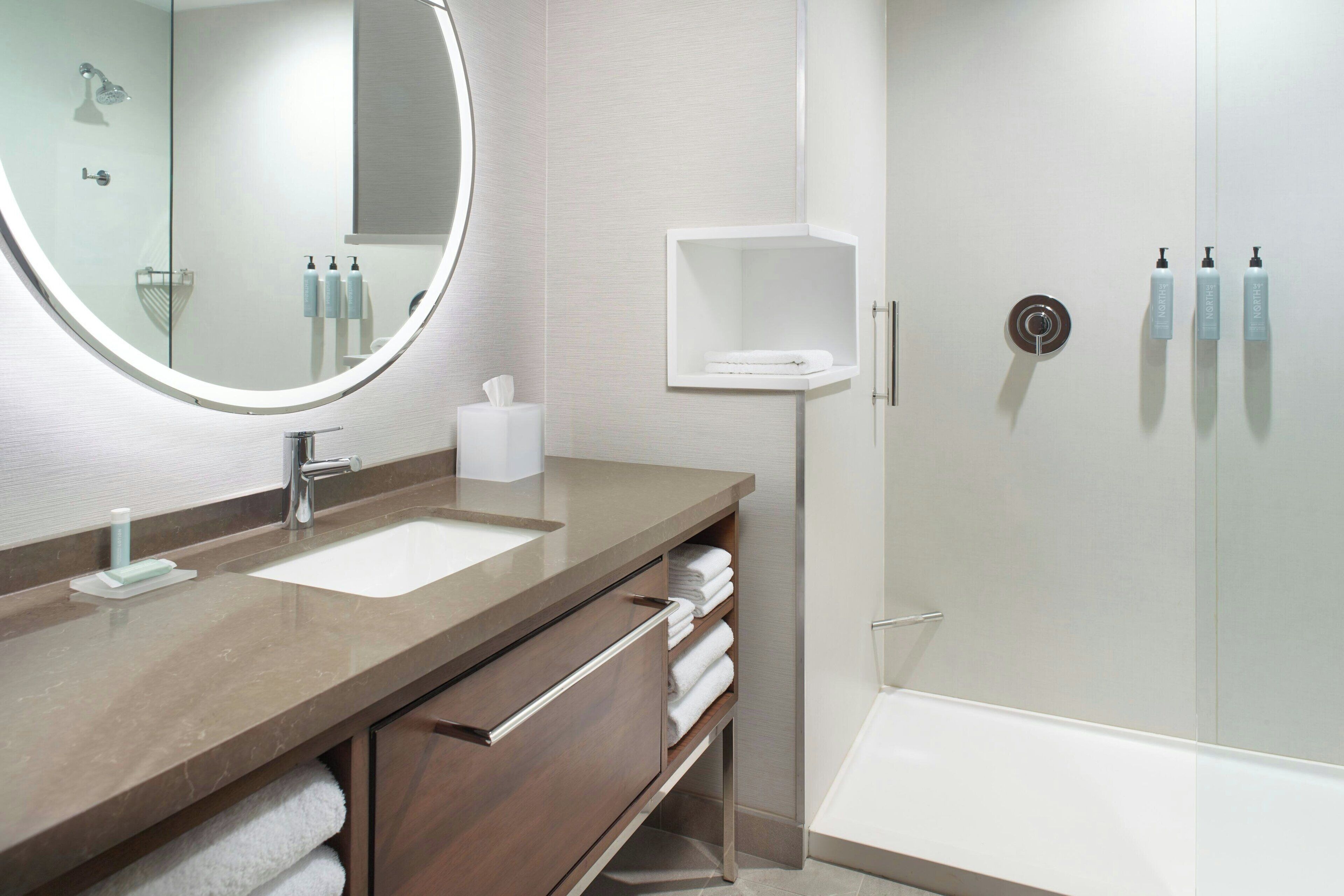 Un baño moderno con un espejo grande, dos lavamanos, una ducha y un tendedero para toallas.