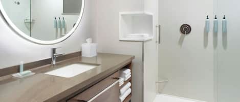 A modern bathroom with a large mirror, two sinks, a shower, and a towel rack.