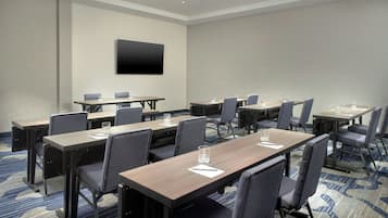 A conference room with multiple tables and chairs, a flat-screen TV mounted on the wall, and a carpeted floor.