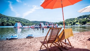 A beach with inflatable water slides, a chair with a yellow towel, and a red umbrella. - Exclusive Secluded Villa: Truffle Oak Forest, Private Pool & Panoramic Lake View (Lissac sur Couze)