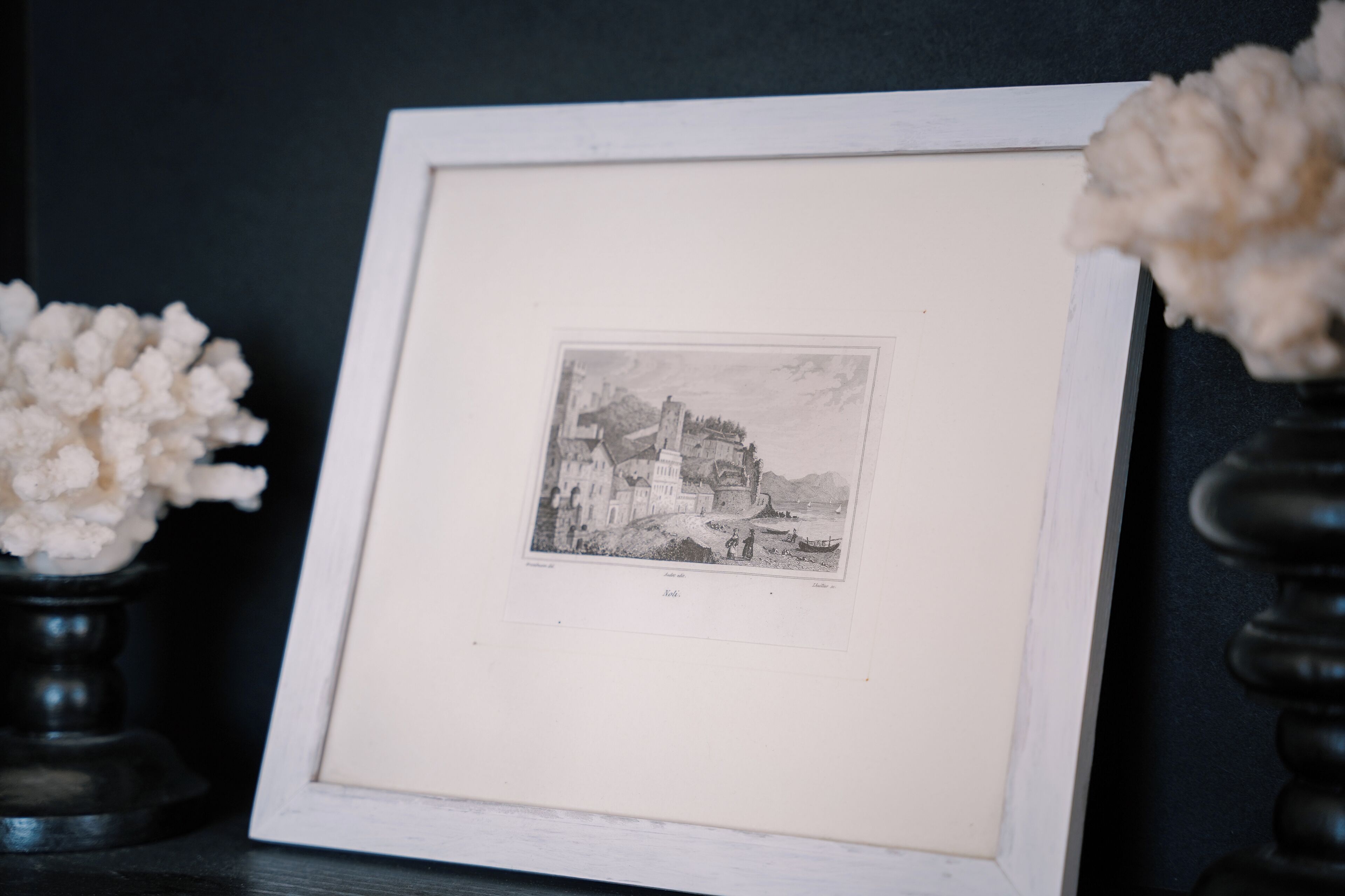 A framed black and white illustration of a coastal town with buildings and a boat.
