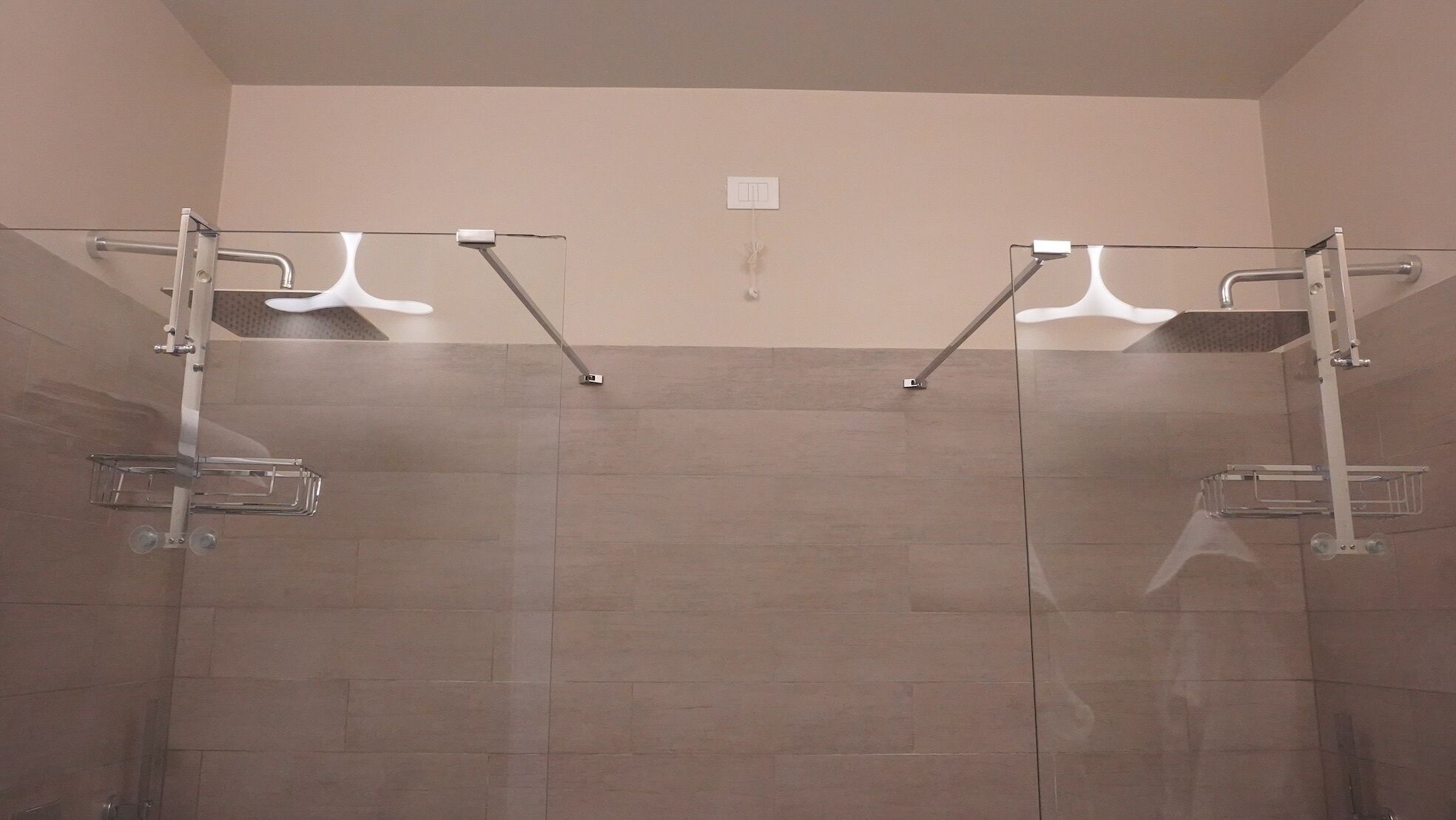 A shower area with two glass-enclosed showerheads and a wall-mounted control panel.