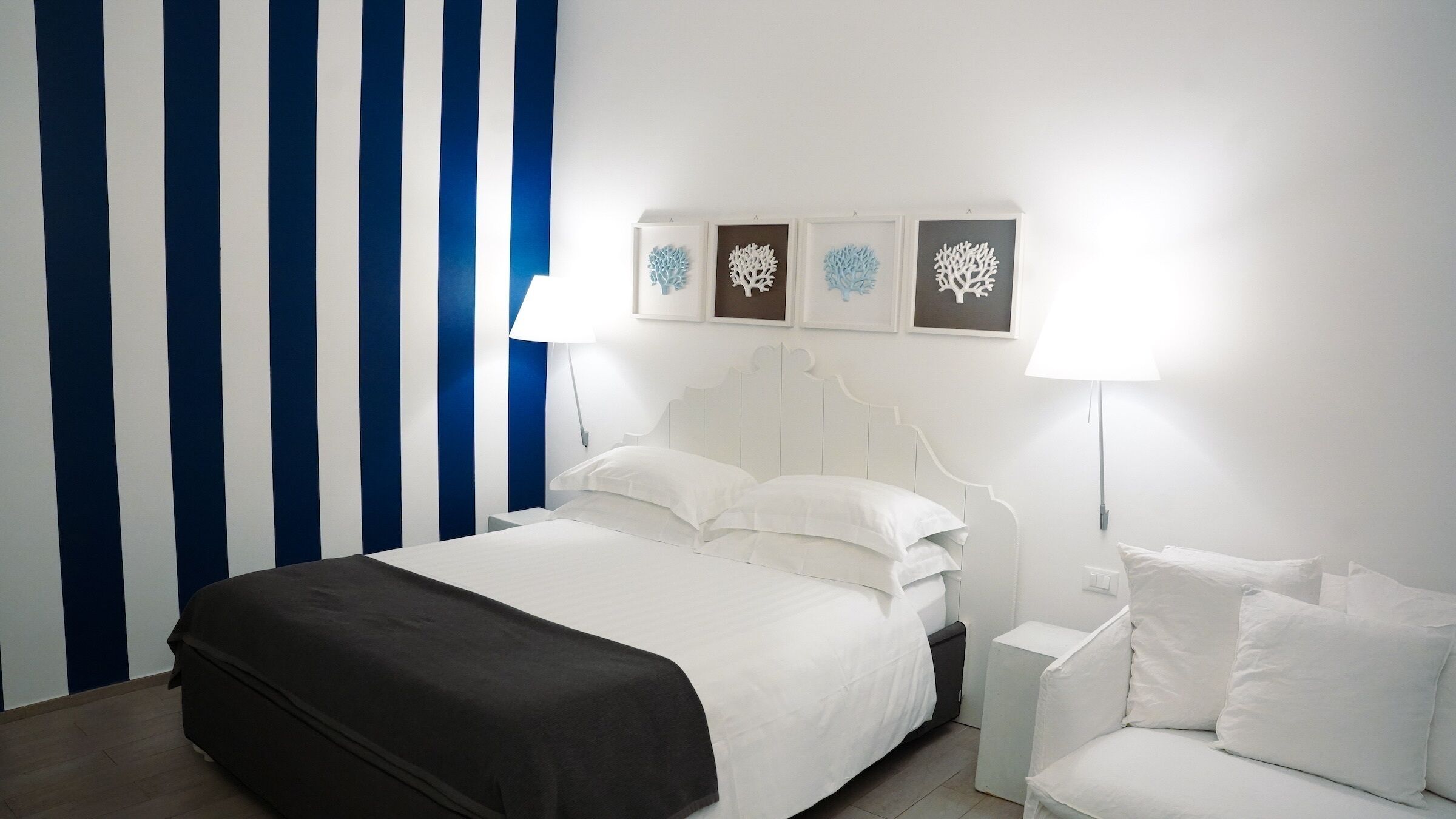 A hotel room with a bed, a bedside table, a lamp, and a wall with striped wallpaper and framed artwork.