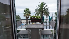Un balcon avec deux chaises et une table, donnant sur une plage bordée de palmiers et offrant une vue sur la mer.