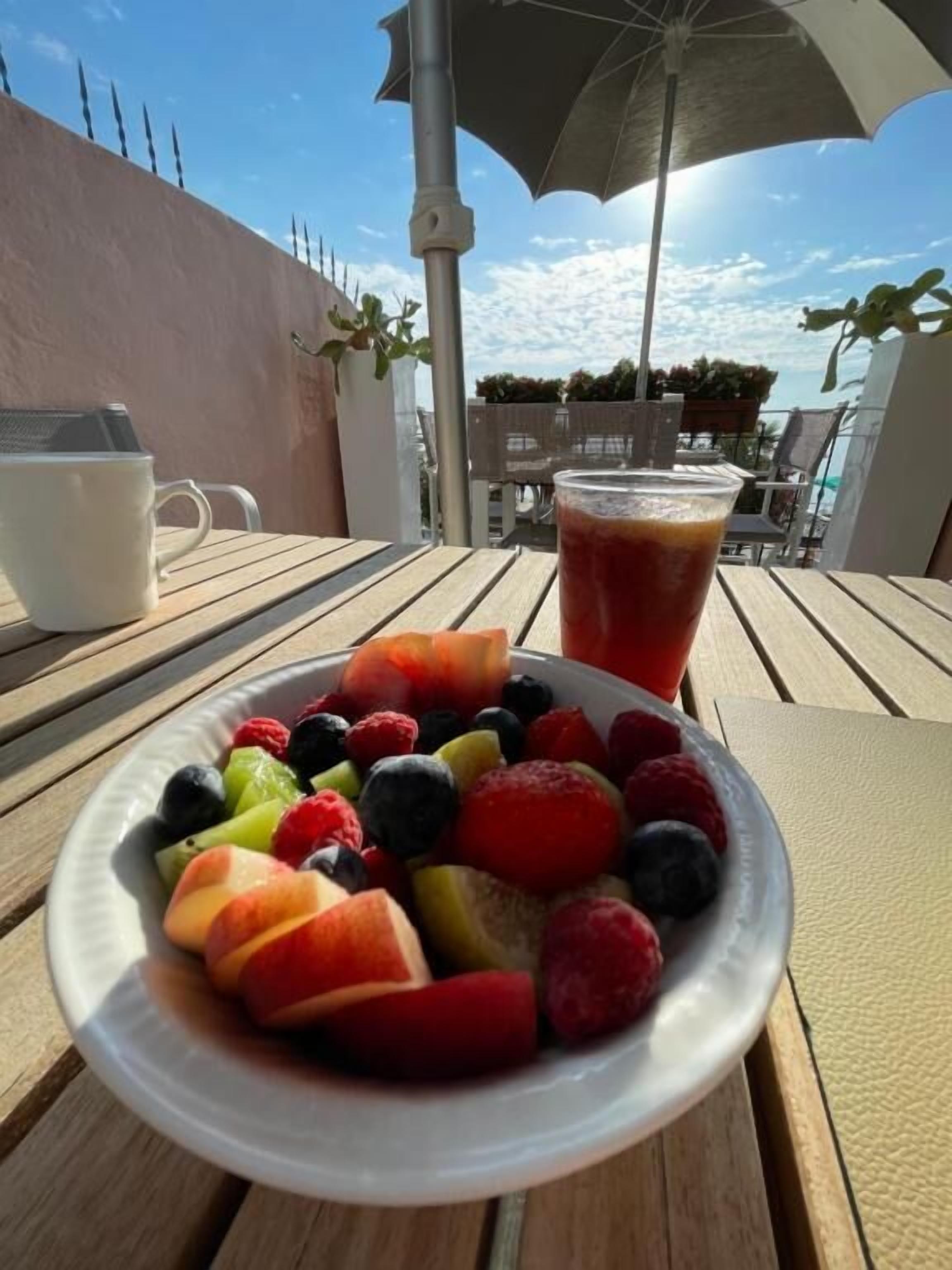 Ein Tisch mit einer Obstplatte und einem Getränk, einem Sonnenschirm und Blick auf den Himmel.