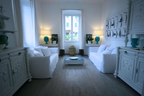 A room with two white sofas, a central coffee table, and a large window with a view of buildings.
