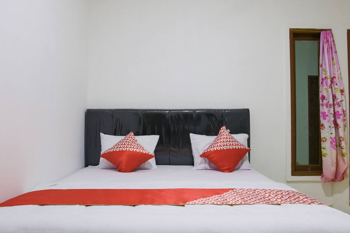 A neatly made bed with white and red bedding, a dark headboard, and two red pillows with a white pattern.