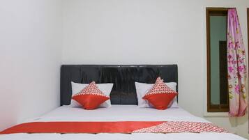 A neatly made bed with white and red bedding, a dark headboard, and two red pillows with a white pattern.