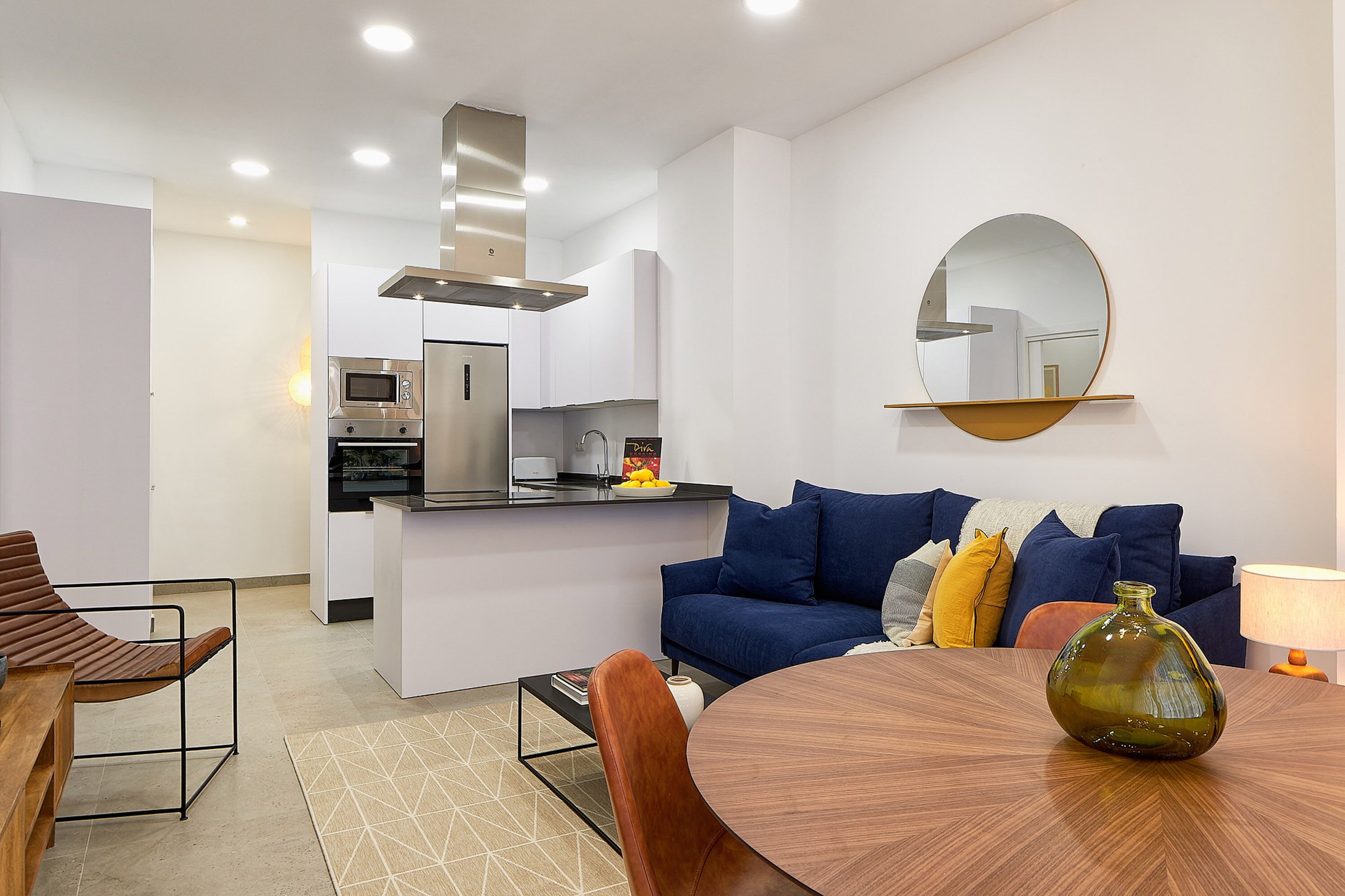 Una cocina moderna con microondas, horno y estufa, un comedor con una mesa redonda y sillas, y un sofá azul con cojines.