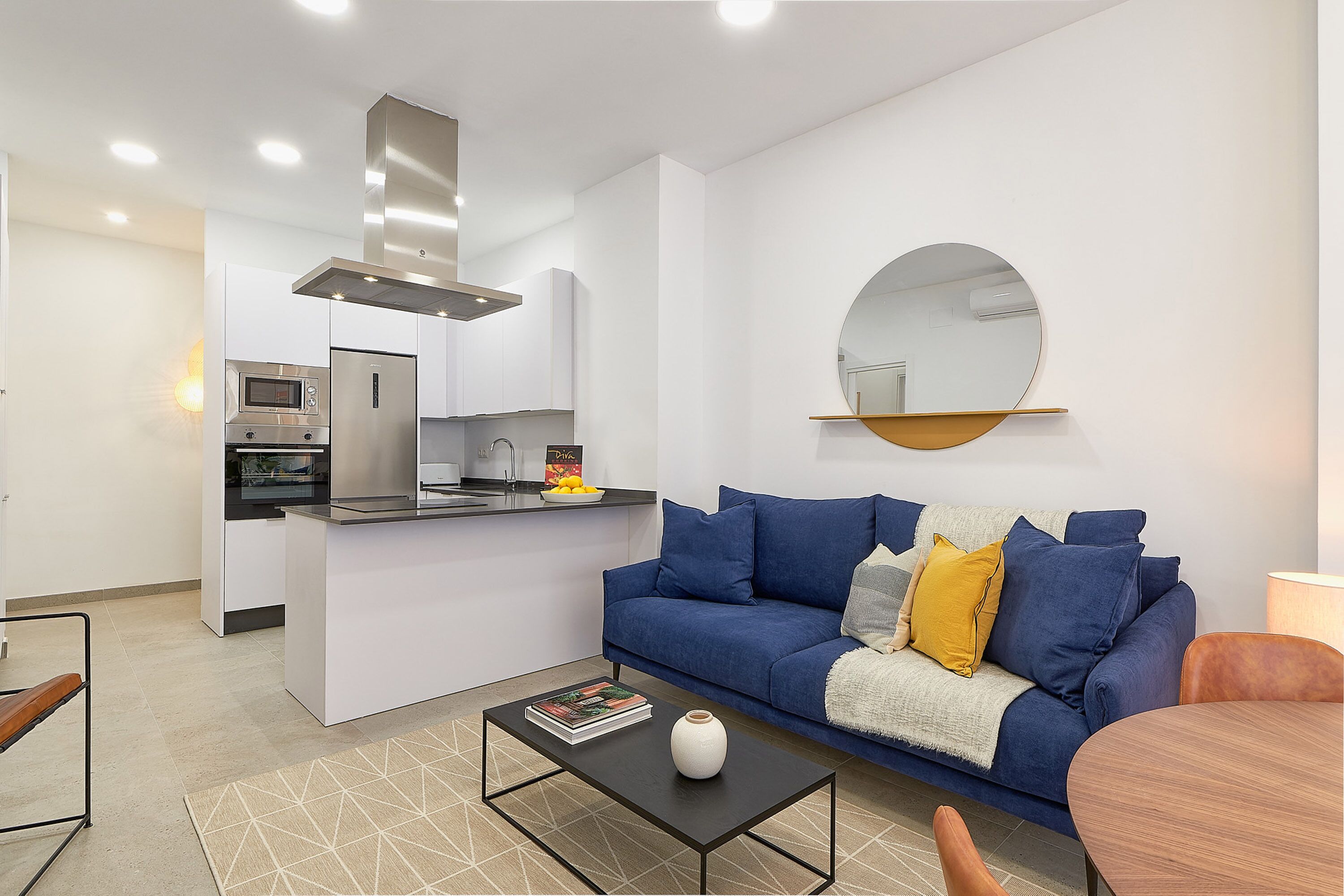 Una sala de estar moderna con un sofá azul, una mesa de centro y una zona de cocina con microondas y estufa.