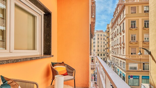 A balcony with wicker furniture, a small table, and a view of adjacent buildings. - Solaga - Soho Suites (Málaga)