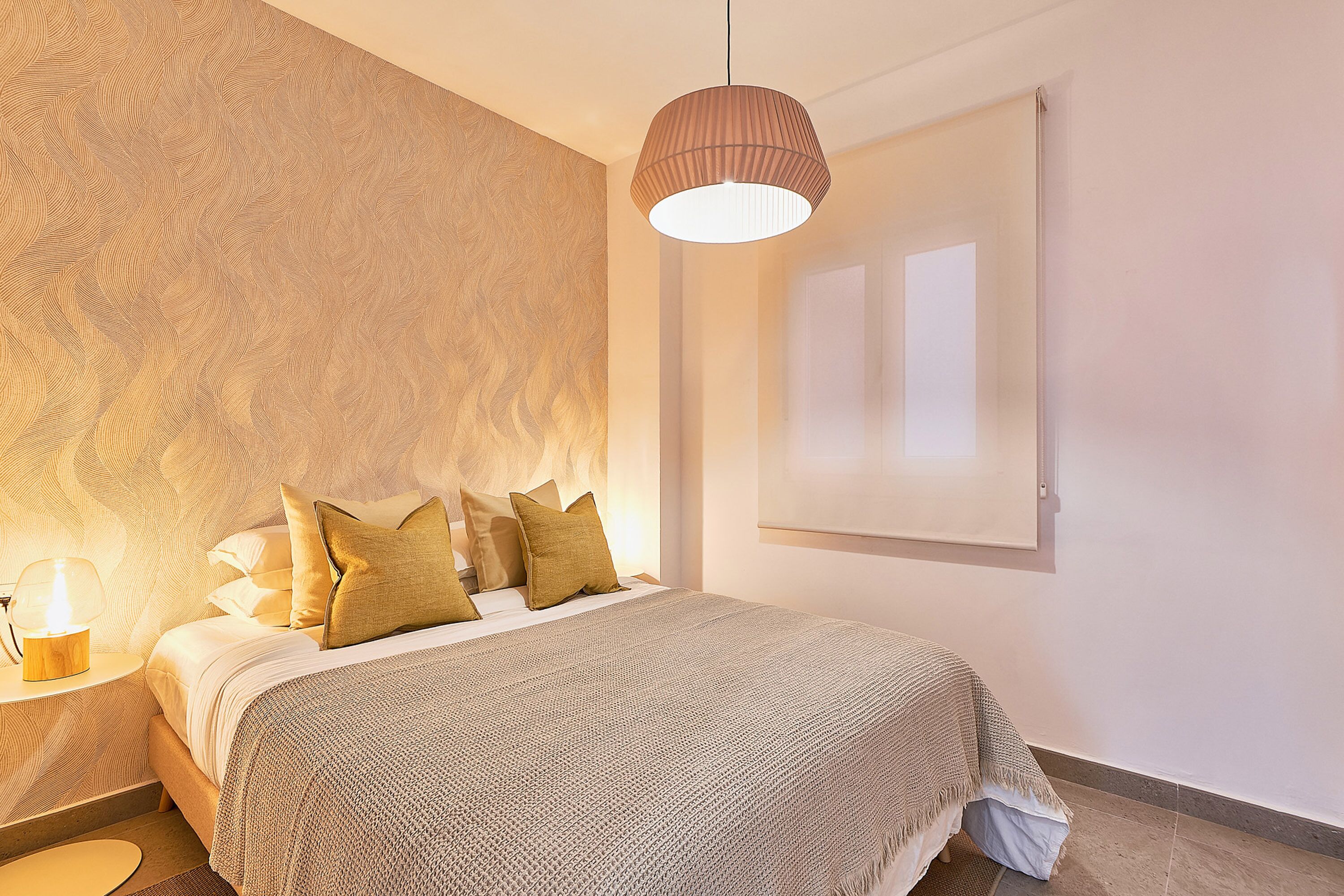A bedroom with a bed, a nightstand, a lamp, and a window.