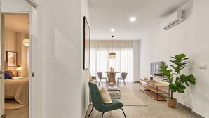 A modern living room with a green armchair, a dining area with a round table, and a large potted plant. - Solaga - Soho Suites (Málaga)