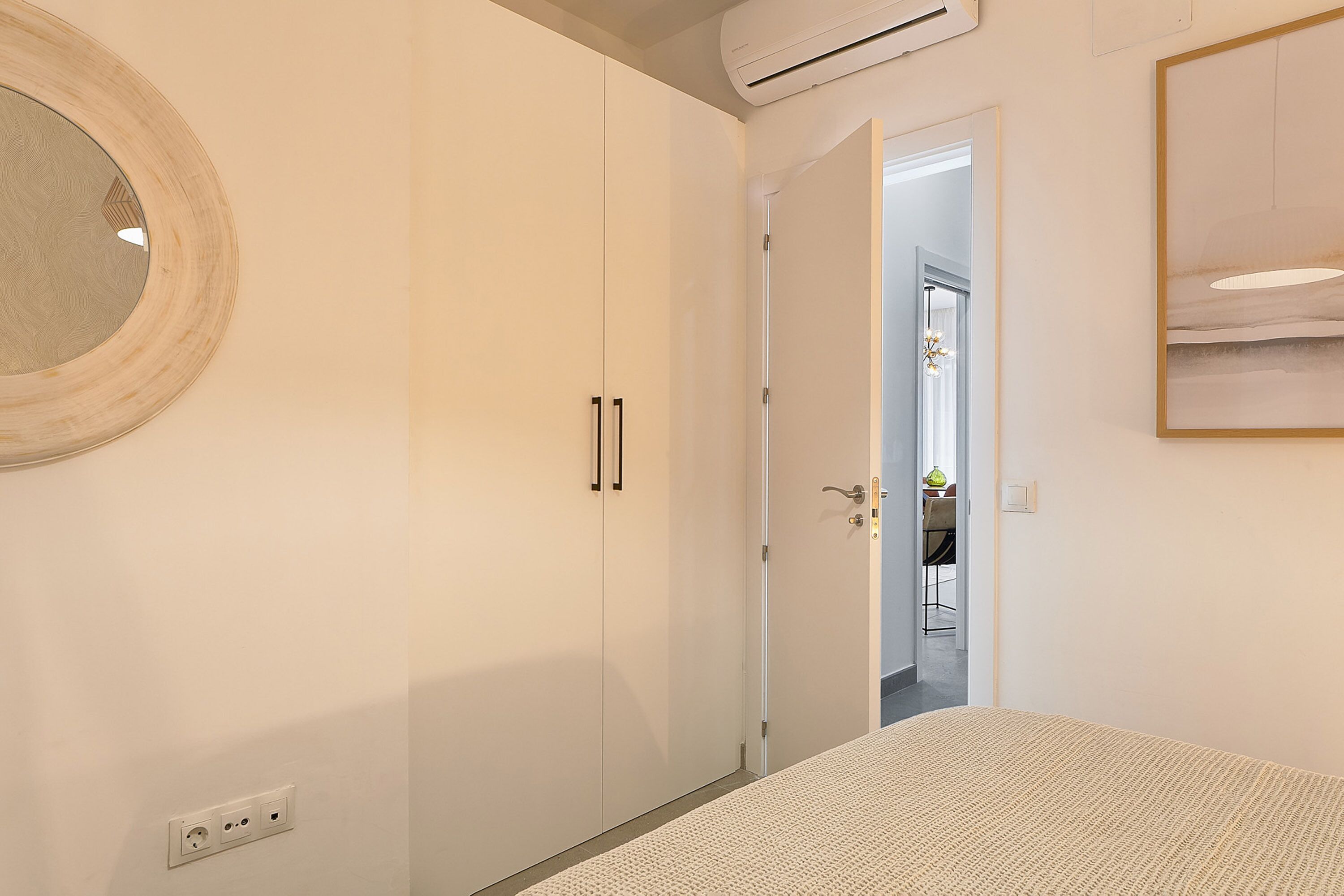 Un dormitorio con cama, armario, espejo y aire acondicionado.