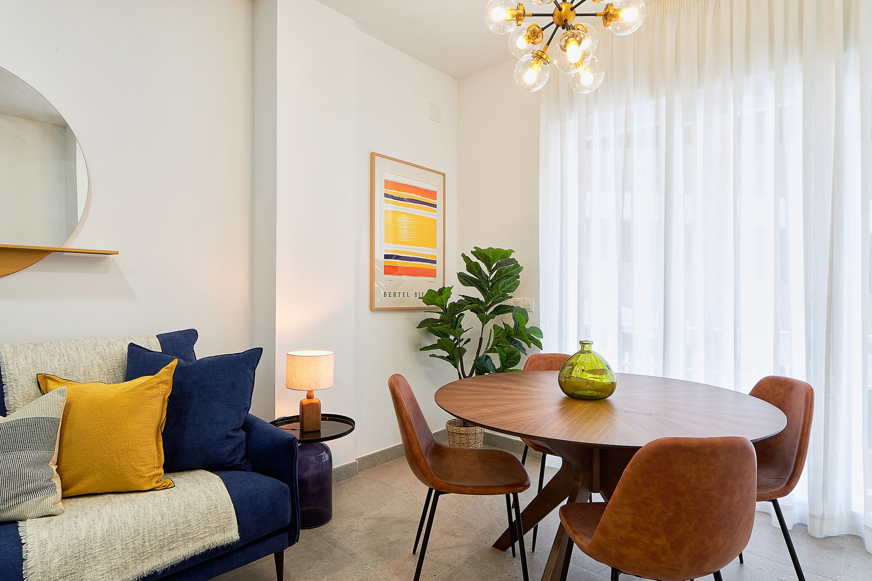 A modern living room with a blue sofa, a round wooden dining table, and brown chairs.