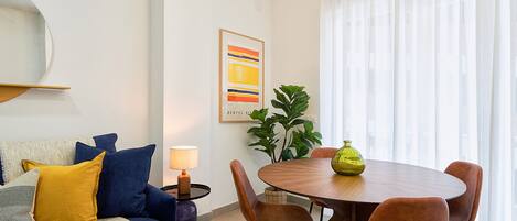 A modern living room with a blue sofa, a round wooden dining table, and brown chairs.