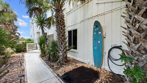 A pathway leading to a white building with a blue door, surrounded by palm trees and a garden area.