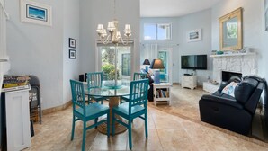 A spacious living room with a fireplace, a dining area with teal chairs, and a TV mounted on the wall.