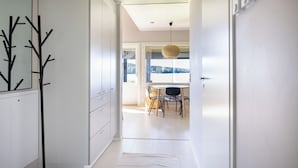 Een moderne keuken met witte kasten, een eethoek met tafel en stoelen, en uitzicht op het groen door grote ramen.