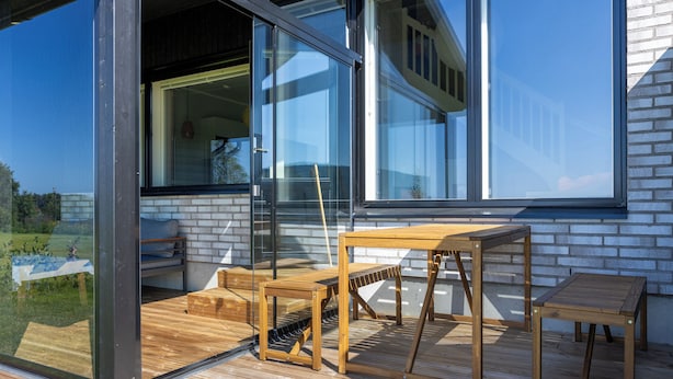 Een modern huis met grote glasramen, houten tuinmeubilair en een gevel van baksteen.