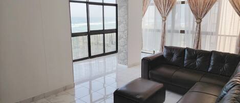 A spacious living room with a large window, a leather sofa, and a matching ottoman.