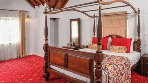 Una cama con dosel de estructura de madera y dosel, una alfombra roja con estampado, y un techo de madera con vigas a la vista.